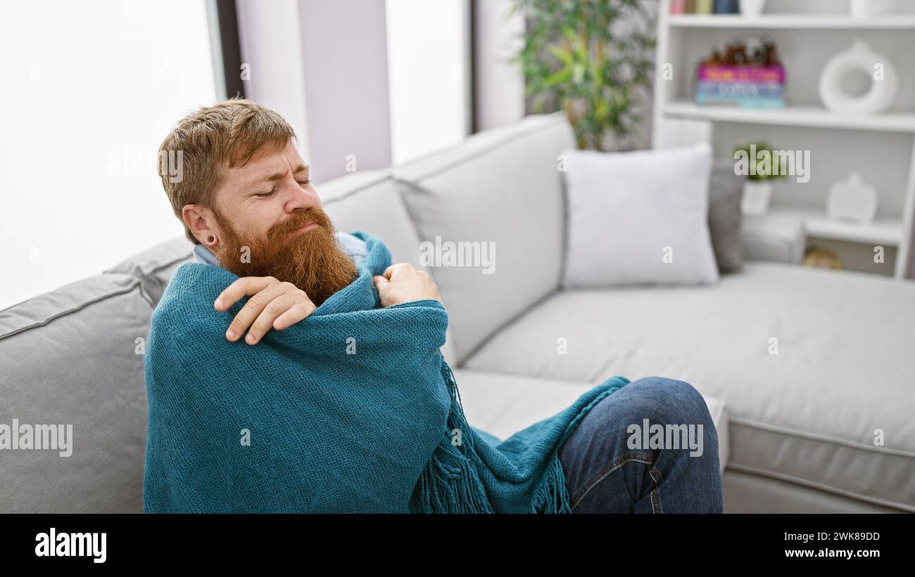 Die Geschichte des kalten Winters, der hübsche junge rothaarige Mann, der friert, findet gemütlichen Komfort in einer warmen Decke, sitzt auf dem Sofa und kämpft zuhause gegen die Kälte. Stockfoto Die Geschichte des kalten Winters, der hübsche junge rothaarige Mann, der friert, findet gemütlichen Komfort in einer warmen Decke, sitzt auf dem Sofa und kämpft zuhause gegen die Kälte. Stockfoto