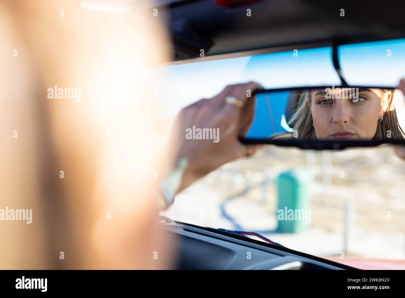 Junge kaukasische Frau stellt den Rückspiegel in einem Auto auf einer Autofahrt ein Stockfoto
