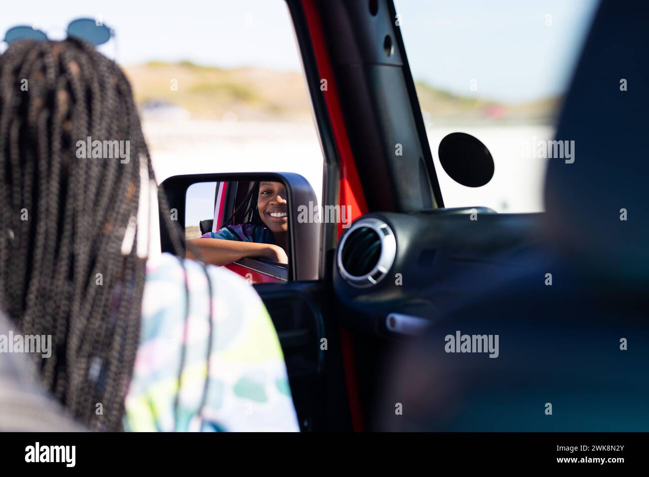 Die junge afroamerikanische Frau lächelt im Auto-Seitenspiegel auf einem Roadtrip Stockfoto