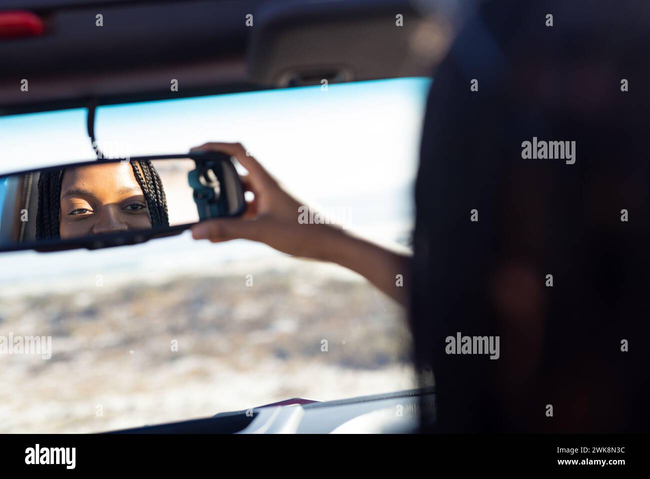 Die junge Afroamerikanerin verstellt den Rückspiegel im Auto auf einem Roadtrip Stockfoto