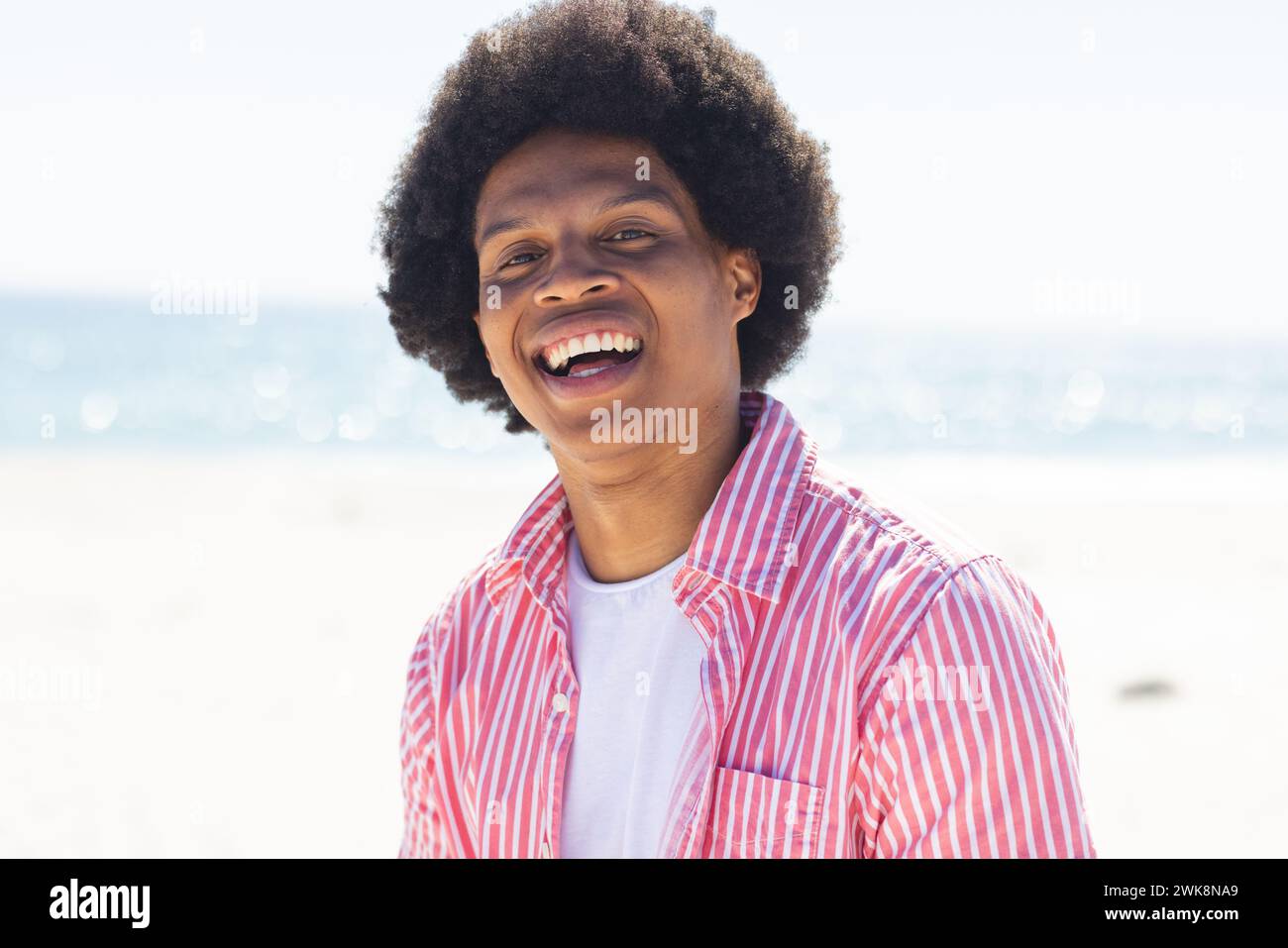 Ein junger Afroamerikaner lächelt draußen am Strand Stockfoto