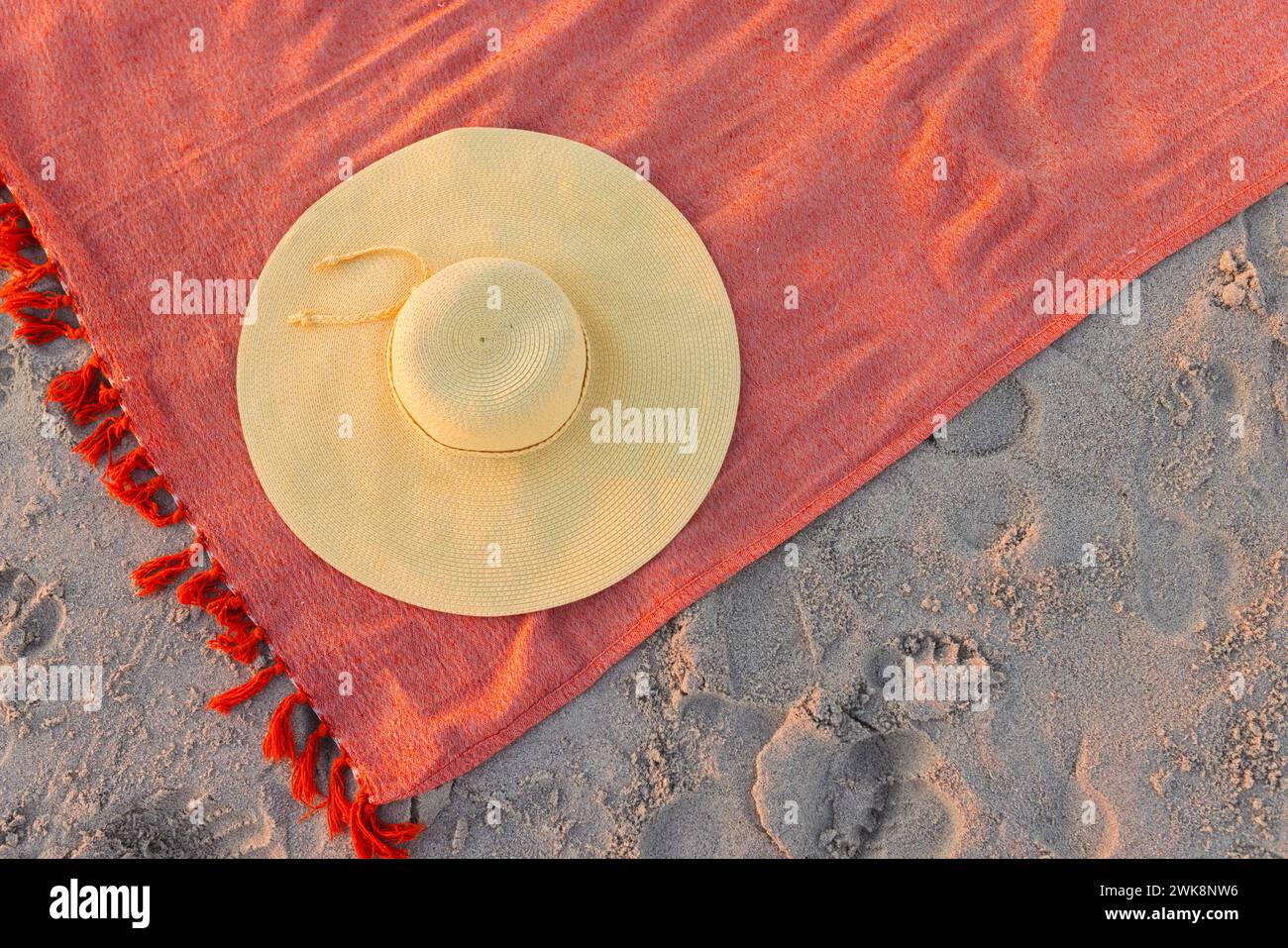 Ein Strohhut liegt auf einem lebendigen Strandtuch mit Kopierraum Stockfoto