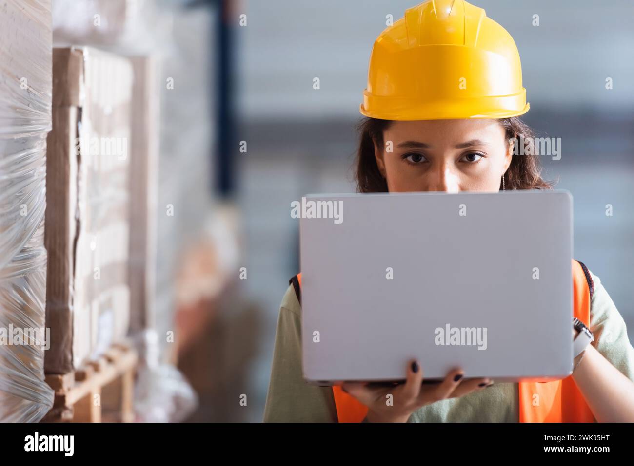 Fokussierte Logistikarbeiterin mit Laptop, die Kamera, Lagerkontrolle und Frachtkontrolle betrachtet Stockfoto
