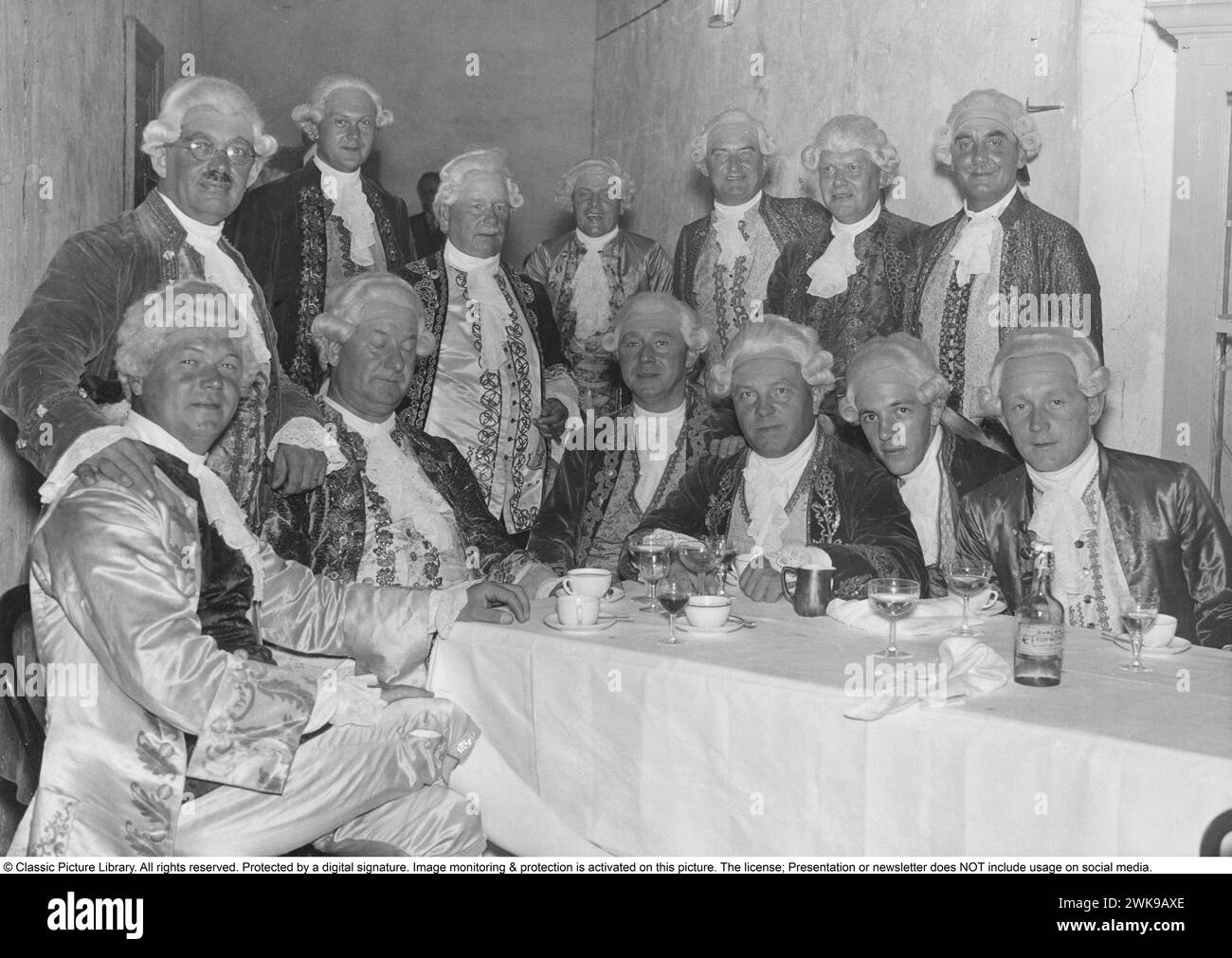 In historischen Kleidern und Perücken. Eine Gruppe von Männern auf einem Foto, das während eines Abendessens im Drottningsholmsteatern aufgenommen wurde, in historischen Kleidern und Perücken gekleidet, während Männer während der Gustavianischen Ära zwischen 1772 und 1809 aussahen und gekleidet waren. 9. Juli 1934 *** Lokale Bildunterschrift *** © Classic Picture Library. Alle Rechte vorbehalten. Geschützt durch eine digitale Signatur. Bildüberwachung und -Schutz ist auf diesem Bild aktiviert. Die Lizenz, Präsentation oder Newsletter beinhaltet KEINE Nutzung in sozialen Medien. Stockfoto