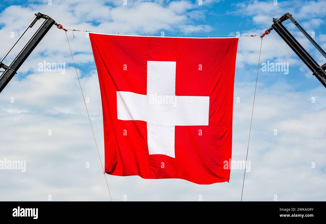 Die Schweizer Flagge gehalten von zwei Kränen, wurde auf den Waffenplatz Kloten-Bülach anlässlich der Connected 2023 aufgehängt. (Kloten, Schweiz, 20. Stockfoto