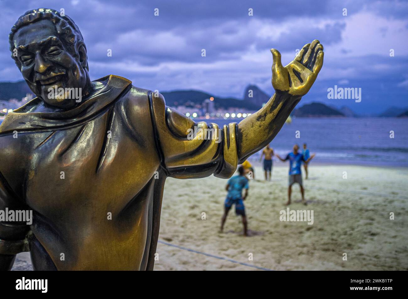 Statue von Dorival Caymmi (30. April 1914 – 16. August 2008) an der Strandpromenade Copacabana, Zuckerhut im Hintergrund, Rio de Janeiro, Brasilien. Caymmi war ein brasilianischer Sänger, Songwriter, Schauspieler und Maler, der mehr als 70 Jahre lang aktiv war. Er trug zur Entstehung der brasilianischen Bossa-nova-Bewegung bei, und einige seiner Samba-Stücke wurden zu Grundfesten der brasilianischen Popmusik. Ebenso bemerkenswert sind seine Balladen, die die Fischer und Frauen von Bahia feiern. Caymmi komponierte etwa 100 Lieder zu seinen Lebzeiten, und viele seiner Werke gelten heute als brasilianische Klassiker. Stockfoto