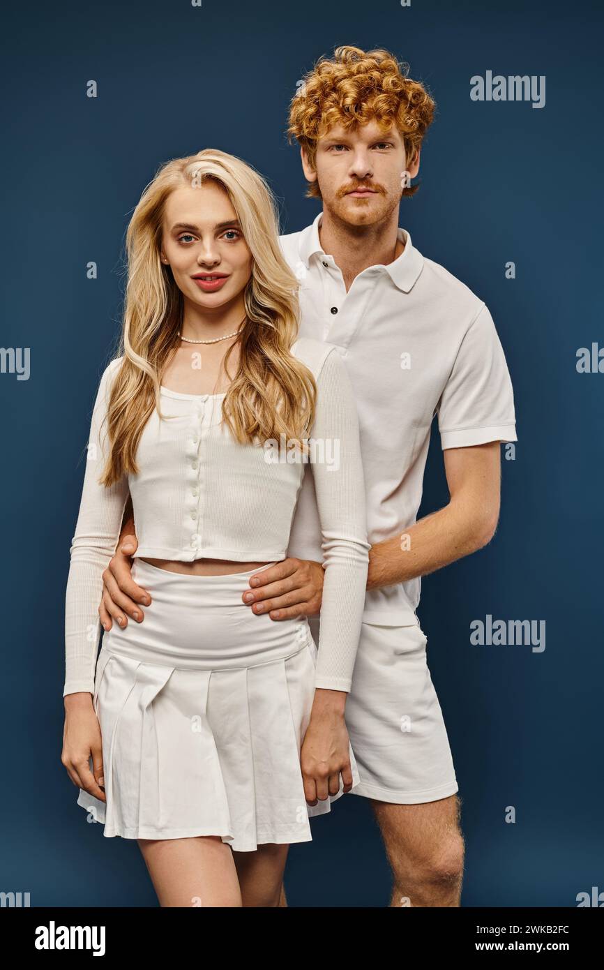 Junges elegantes Paar in alten Geldkleidern, die auf die Kamera vor blauem Hintergrund blicken, zeitlose Mode Stockfoto