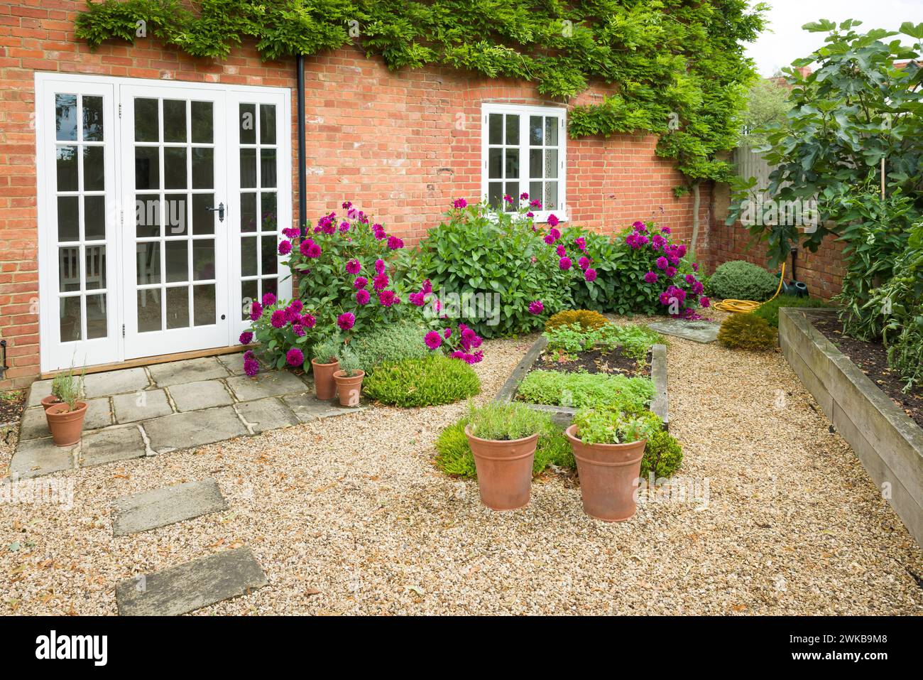 Britisches Haus und Garten mit Terrasse und Glastüren. Cottage oder Innenhof Garten (Hinterhof) mit Kies und Yorker Steinpflaster Stockfoto