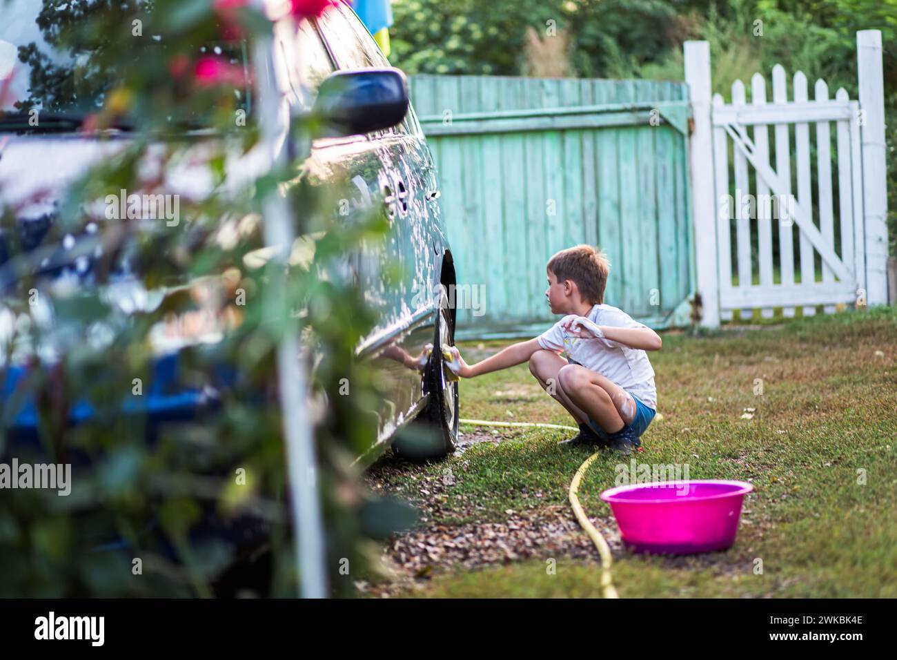Teenager, der Autoräder mit Waschlappen mit Seife wäscht. Das Konzept des Lernens durch praktische Übungen Stockfoto