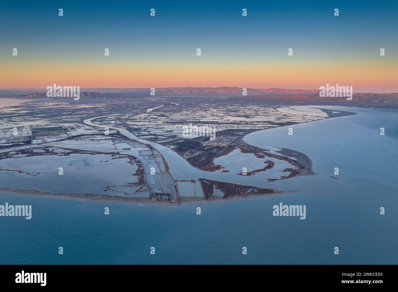 Sonnenaufgang über der Mündung des Ebro-Flusses im Ebro-Delta mit dem Vollmond am Horizont. Luftaufnahme (Ebro Delta, Tarragona, Katalonien, Spanien) Stockfoto