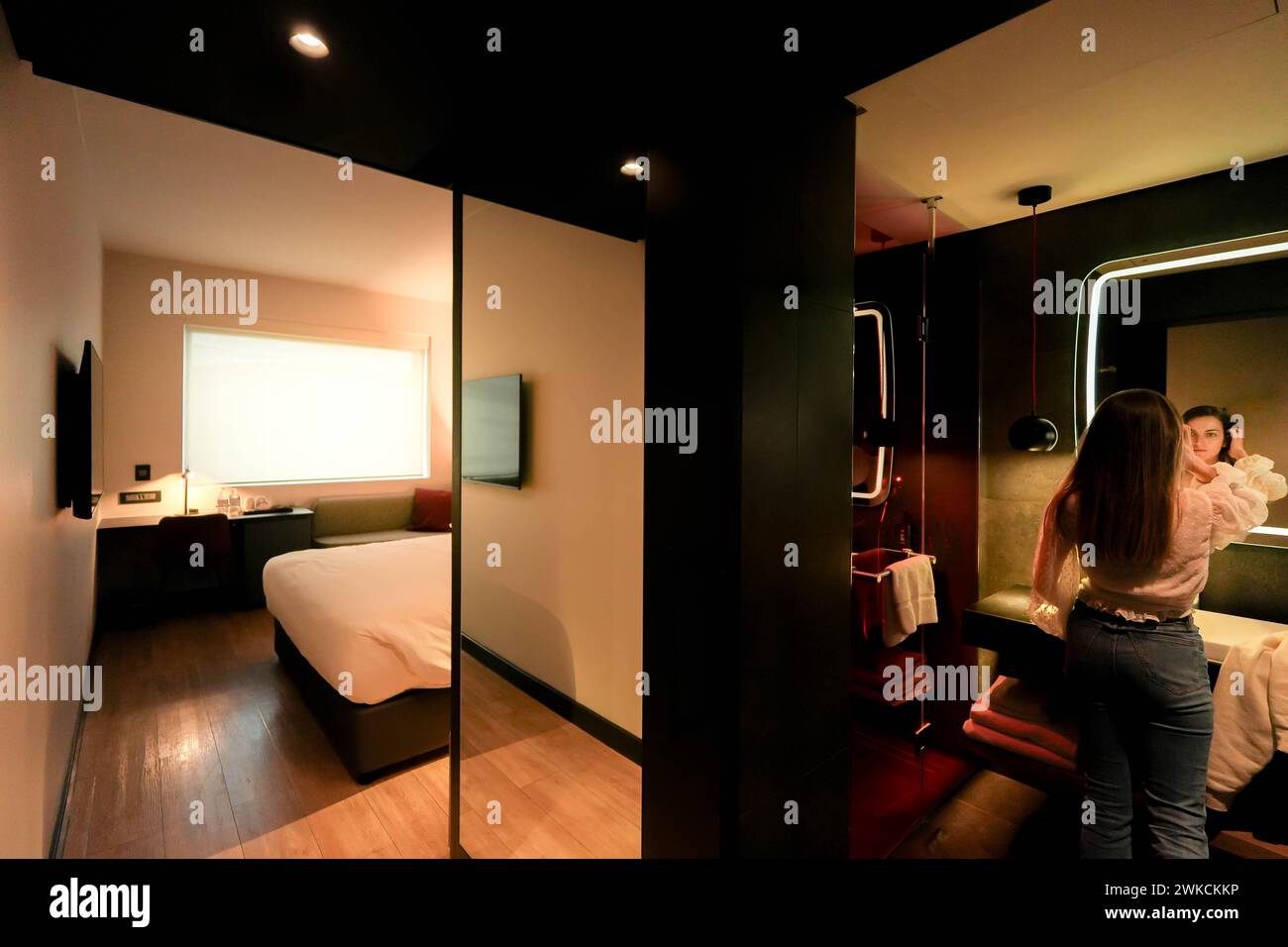 Ein Gast steht in einem modernen Hotelzimmer mit minimalistischem Dekor, in einem Moment des Komforts und der Eleganz. Stockfoto