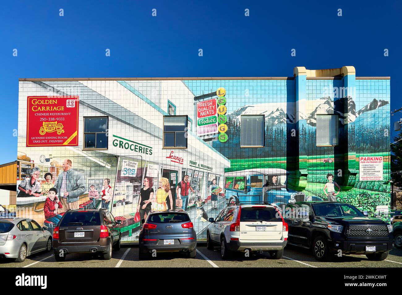 Ein helles Wandgemälde an der Seite eines Lebensmittelgeschäfts, das Menschen zeigt, die in einem Geschäft einkaufen. Autos stehen vor dem Wandgemälde. Stockfoto