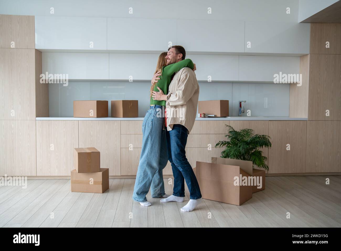 Liebevoller Mann, der die geliebte Frau umarmt, zieht neue Traumwohnung. Lassen Sie sich von Familienpaaren am Umzugstag verwöhnen. Stockfoto