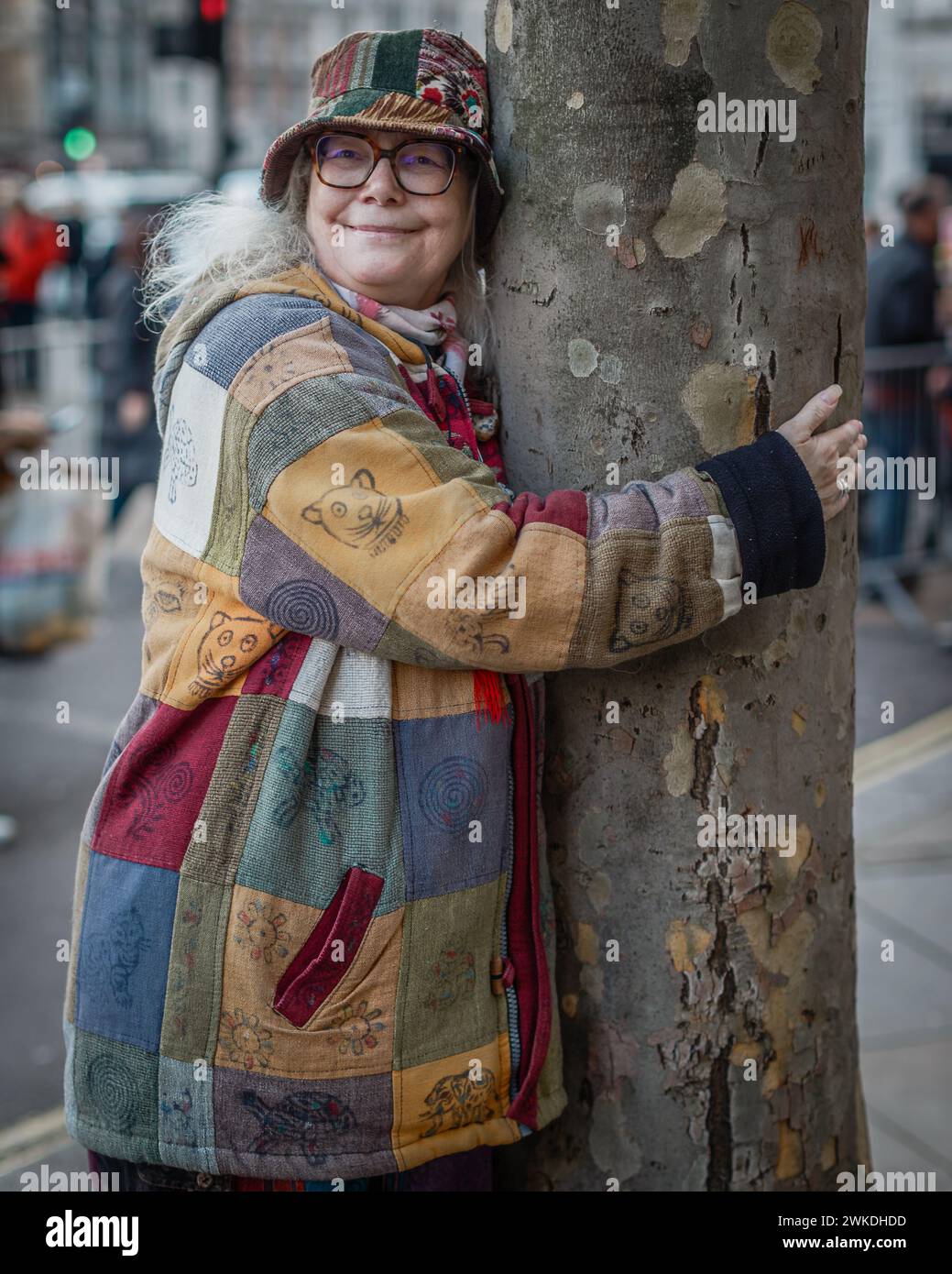 Eine bunt gekleidete Frau umarmt einen Baum in London. Stockfoto