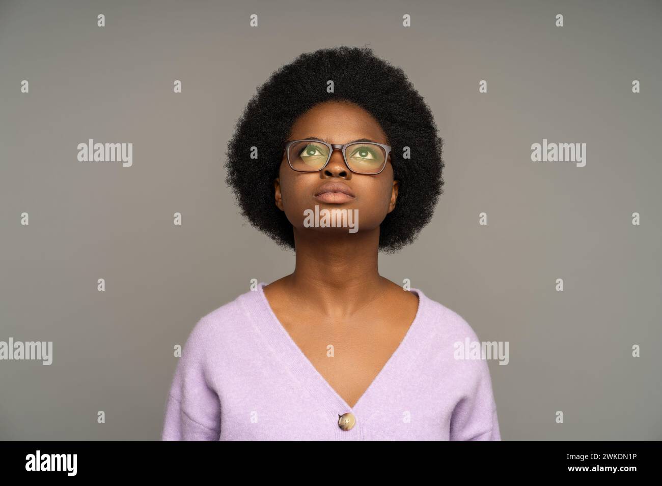 Nachdenkliche nachdenkliche afroamerikanische Frau, die aufmerksam nach oben blickt, isoliert auf Studiohintergrund Stockfoto