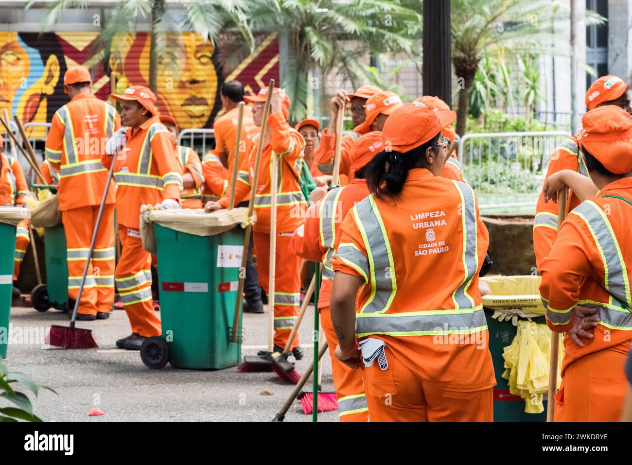 In Sao Paulo, Brasilien, sitzen einige Sanitärangestellte in markanten orangefarbenen Uniformen auf einer Bordsteinkante Stockfoto