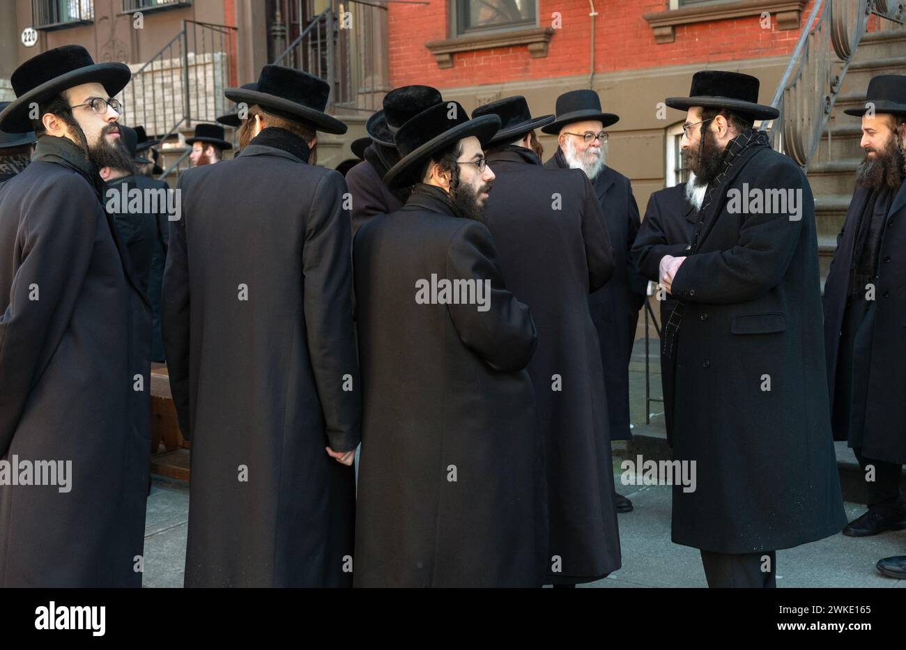 Orthodoxe jüdische Männer versammeln sich vor einem Privathaus und warten darauf, dass Familiendienste beginnen. In Brooklyn, New York, Winter 2024. Stockfoto