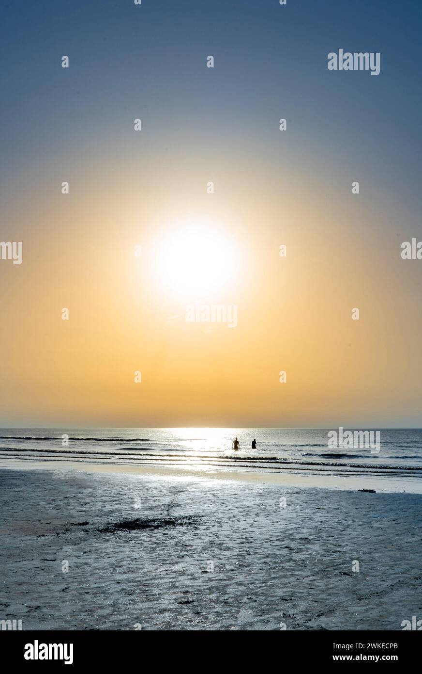 Niedrige Sonne auf dem Meer von de panne mit der Silhouette von zwei Personen und dem Meer Stockfoto