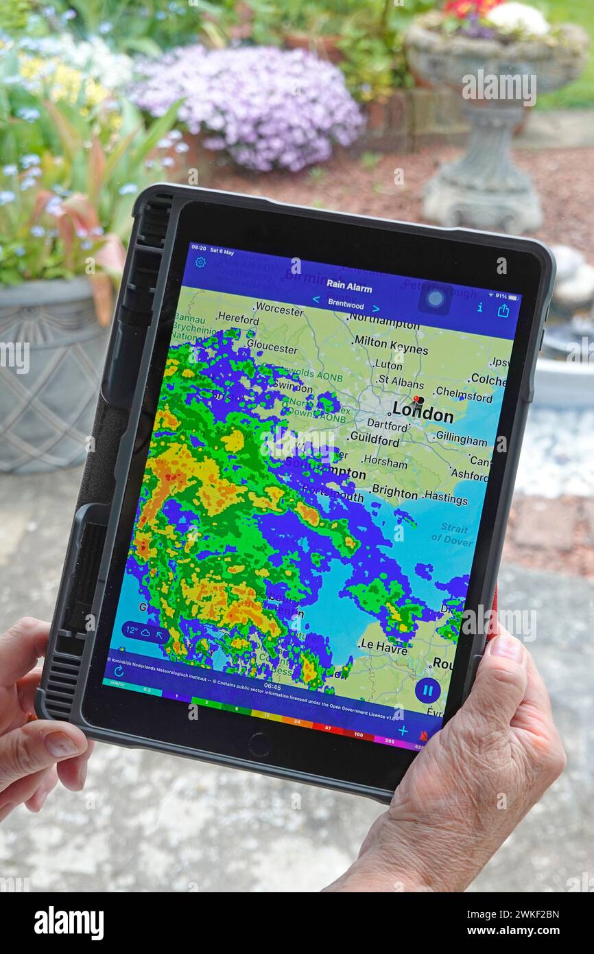 Frau Hände halten Apple ipad pro Tablet Regenalarm App und Echtzeit Farbradar Datenschicht des Niederschlags lokale Karte nasses Wetter auf dem Home Window Essex UK Stockfoto