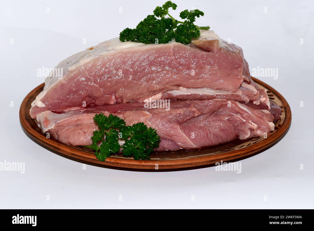 Auf dem Bild liegen ein Stück Schweinefleisch und Zweige eines duftenden Hahns auf einer Tonplatte. Stockfoto