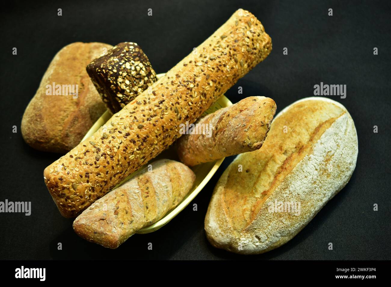 Baguettes verschiedener Länge befinden sich in einem Korb, und auf einem dunklen Tisch befindet sich ein Brötchen mit einer gerissenen Oberfläche. Stockfoto