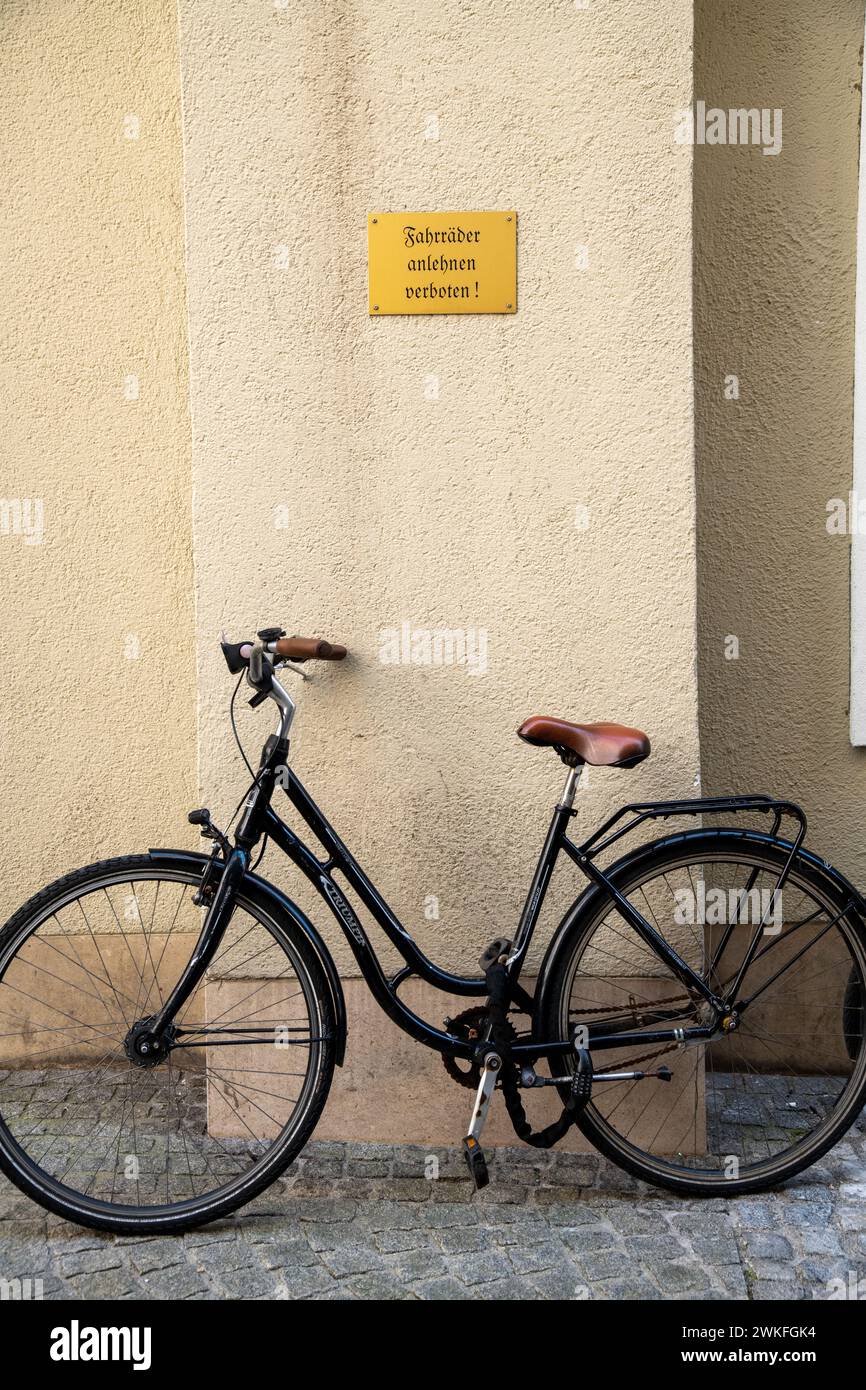 Ein Fahrrad, das sich an eine gelbe Hauswand lehnt und unter einem gelben Schild mit der deutschen Inschrift in alten Buchstaben verschlossen ist: Fahhrad anlehnt verboten Stockfoto