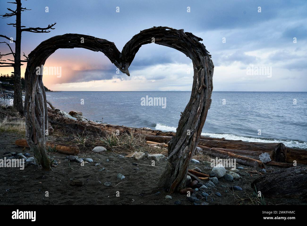 Ein großes Driftood-Herz, das als Rahmen für Fotos von Menschen in der Abenddämmerung an einem Meeresstrand verwendet wird. Stockfoto