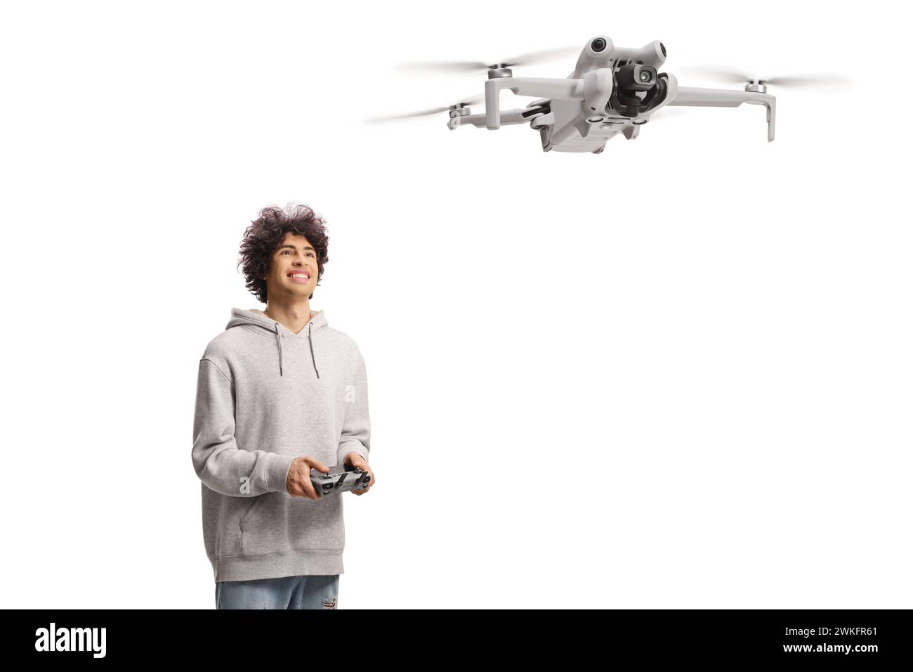 Glücklicher junger Mann, der eine Drohne mit einem Cotroller-Gerät fliegt und isoliert auf weißem Hintergrund aufblickt Stockfoto