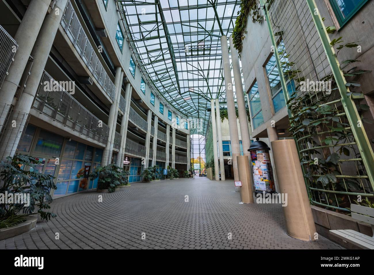 Warschau, Polen - 14. Oktober 2023: Innenraum des großen Platzes des Universitätsbibliotheksgebäudes mit hohen Säulen, Blumen, Geschäften und Glasdecke Stockfoto