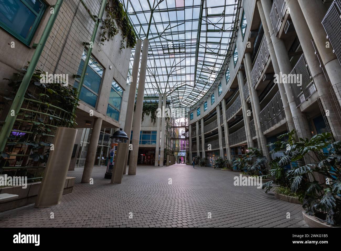 Warschau, Polen - 14. Oktober 2023: Innenraum des großen Platzes des Universitätsbibliotheksgebäudes mit hohen Säulen, Blumen, Geschäften und Glasdecke Stockfoto