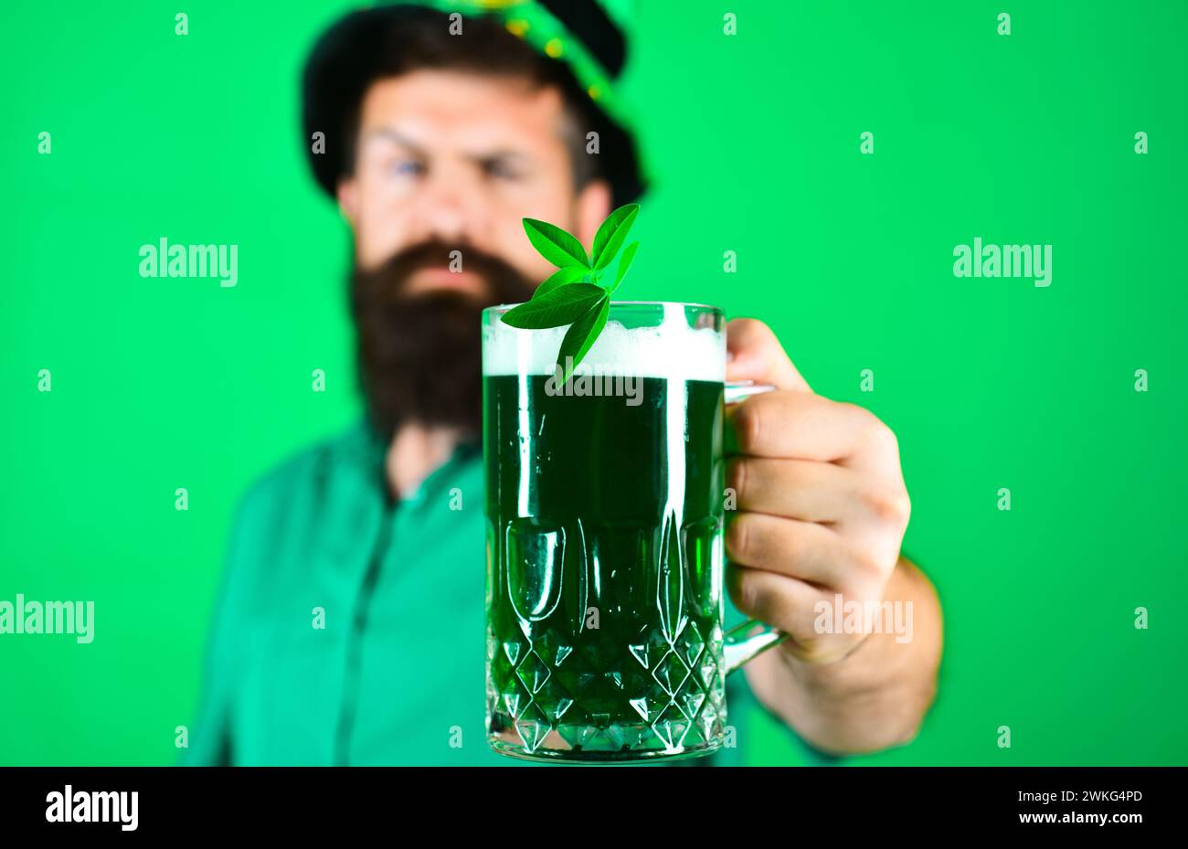 Patrick's Day Pub Party Party Party. Selektiver Fokus auf Becher grünes Bier mit Klee in der Hand eines bärtigen Mannes. Irland Tradition. Traditionelles Irisch Stockfoto