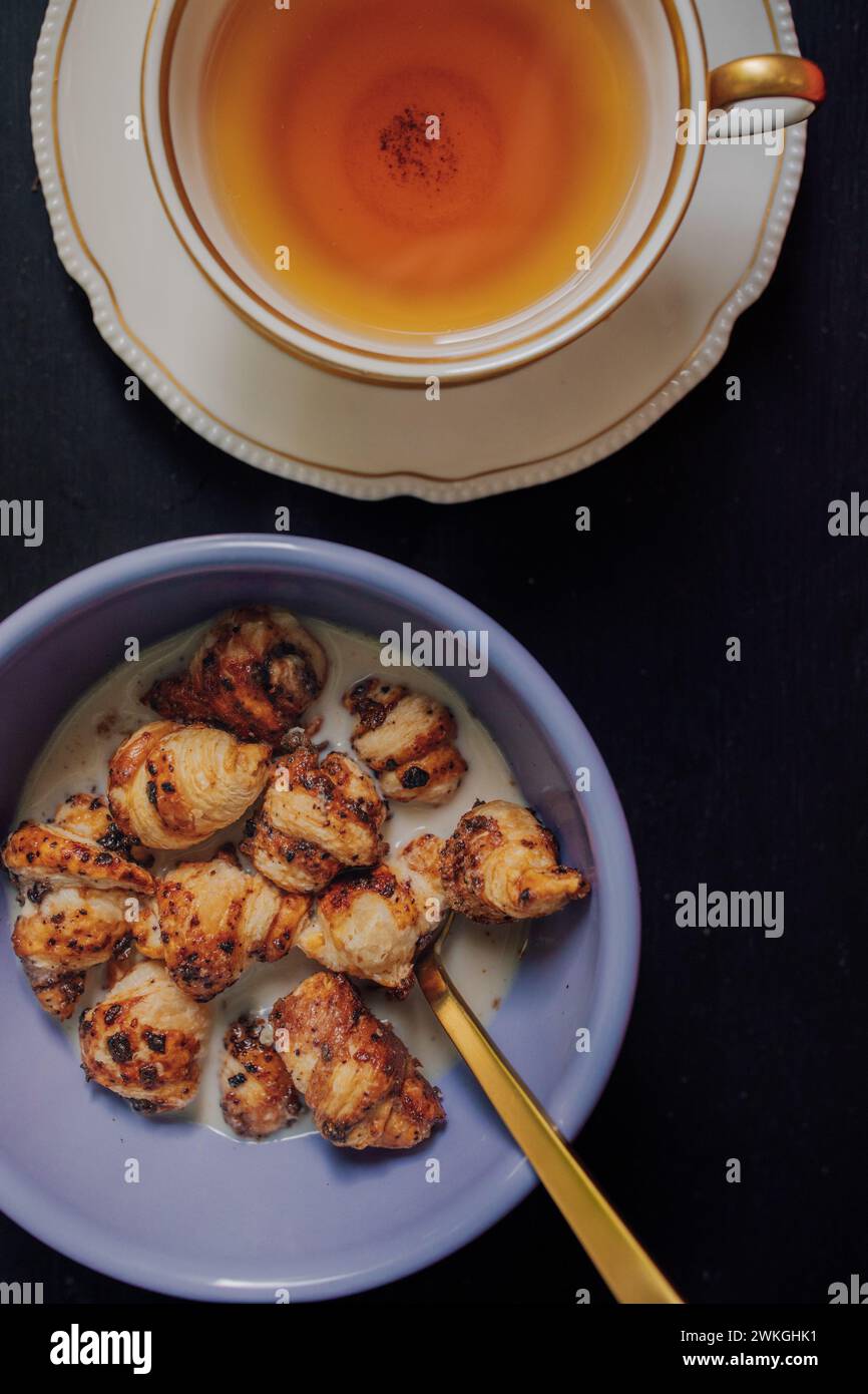 Lila Schüssel mit Mini Croissant Müsli und goldenem Löffel auf silbernem Tablett Stockfoto