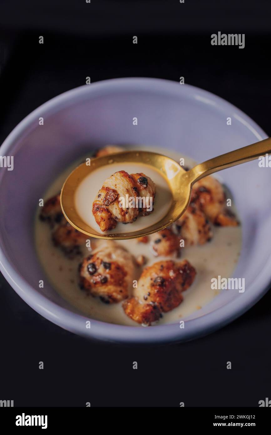 Lila Schüssel mit Mini Croissant Müsli (mit Blaubeerzucker) und goldenem Löffel auf schwarzem Tisch Stockfoto