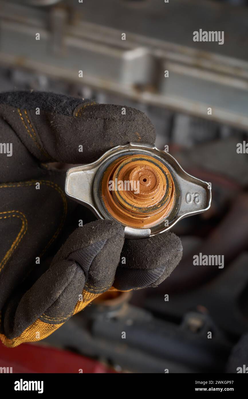 Nahaufnahme eines Mechanikers, der einen alten rostigen und schlammigen Kühlerdeckel hält, Rostansammlungen auf dem Kühler, Probleme im Kühlsystem des Autos wie Überhitzung Stockfoto
