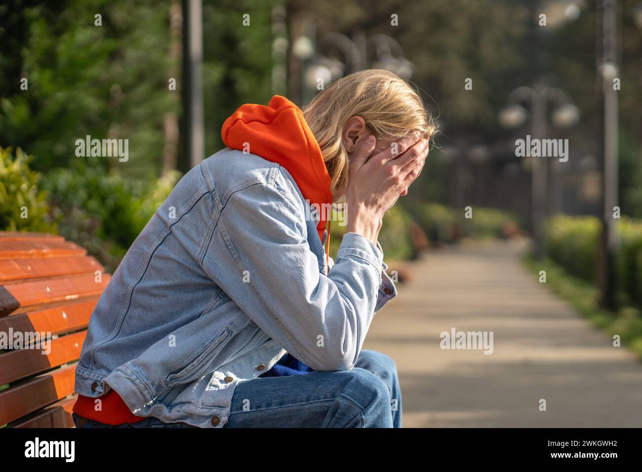 Trauriger Hipster-Typ sitzt auf der Bank, schließt das Gesicht mit den Händen, weint über gebrochene romantische Beziehungen Stockfoto