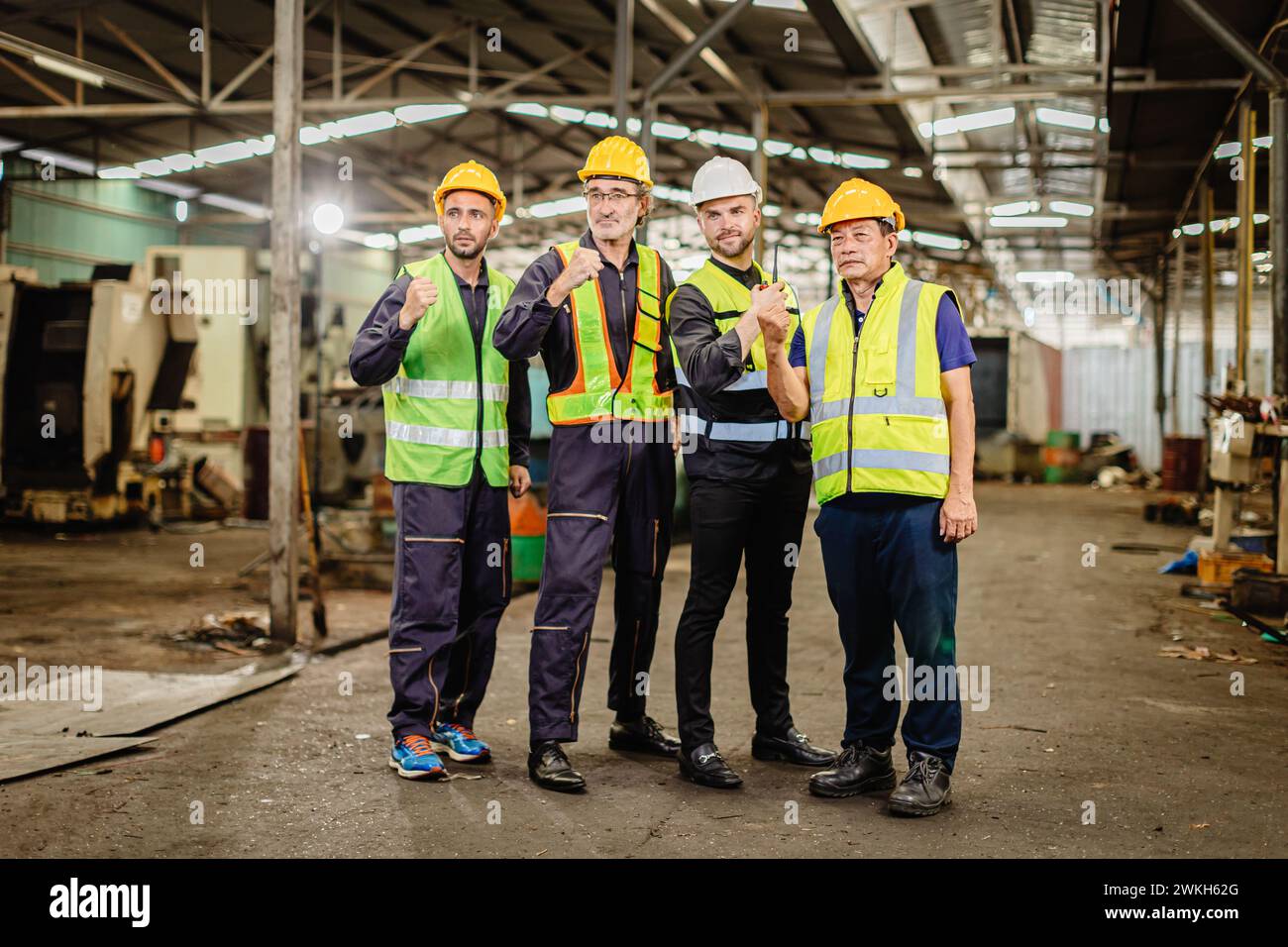 Ein männliches Ingenieurteam, das in der Schwerindustrie arbeitet, steht zusammen. Eine Gruppe professioneller Mitarbeiter arbeitet glücklich und selbstbewusst zusammen. Stockfoto