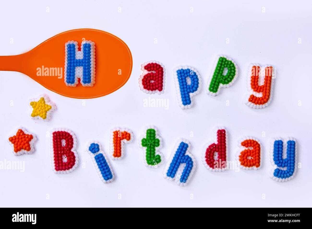 Happy Birthday geschrieben mit bunten Zuckerbuchstaben und einem orangen Löffel Stockfoto