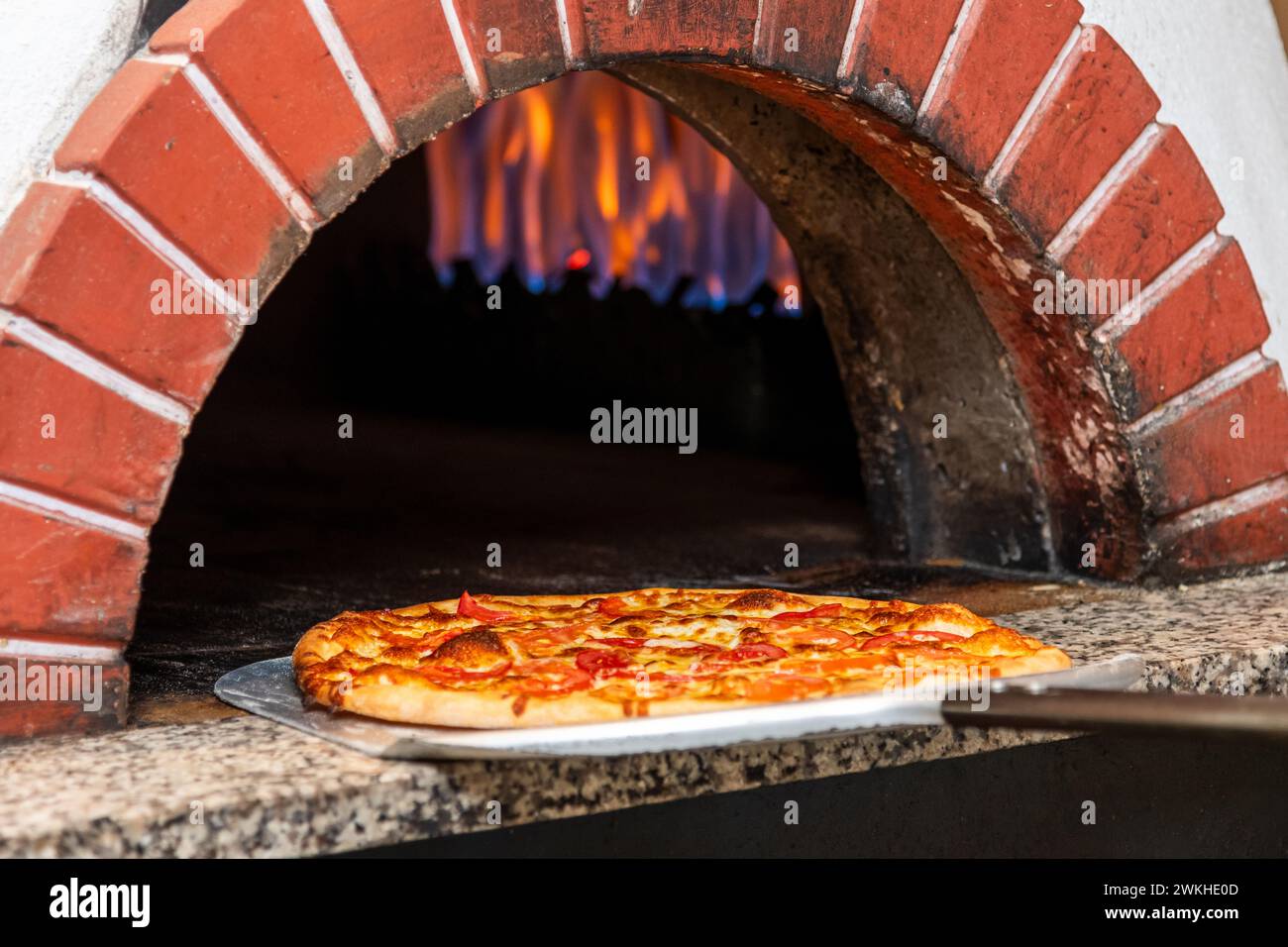 Gemischte Pizza frisch aus dem Pizzaofen mit sichtbaren Flammen im Hintergrund Stockfoto