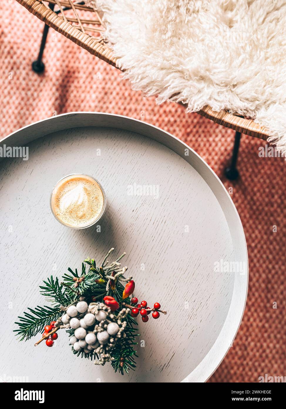 Ein skandinavisches Weihnachtsgesang mit Kaffee, stechpalmen- und Kiefernlaub und einem flauschigen, mit Haut bedeckten Stuhl Stockfoto