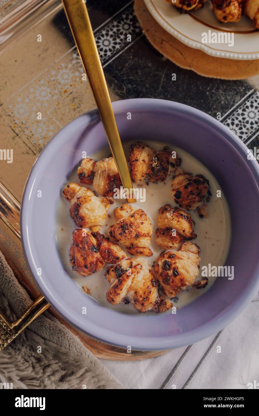 Lila Schüssel mit Mini Croissant Müsli und goldenem Löffel auf silbernem Tablett Stockfoto