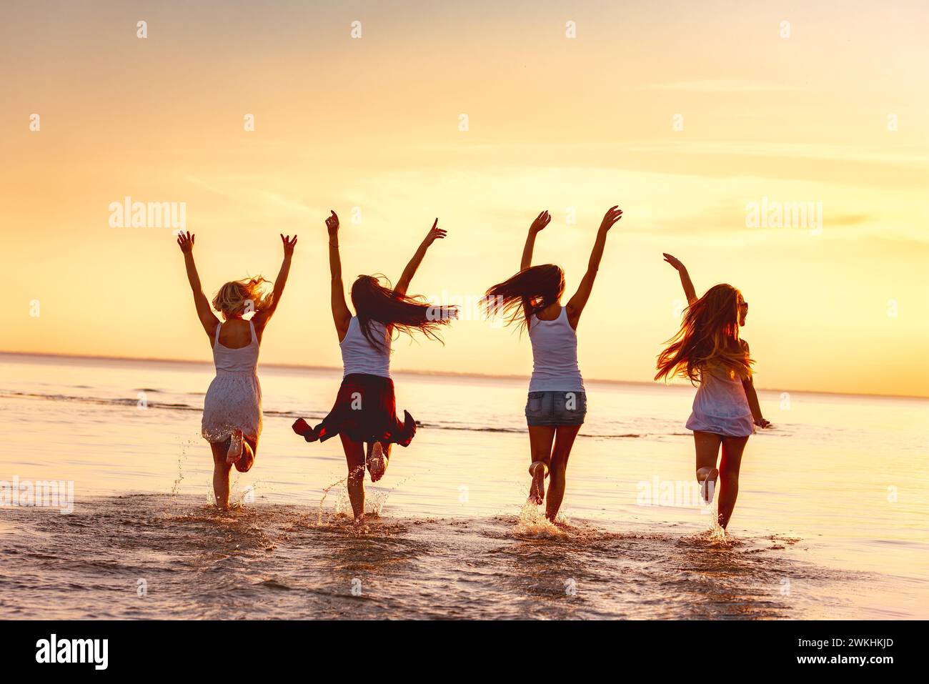 Eine Gruppe fröhlicher Mädchen läuft am ruhigen Sonnenuntergangsstrand eines Sees im flachen Wasser entlang Stockfoto