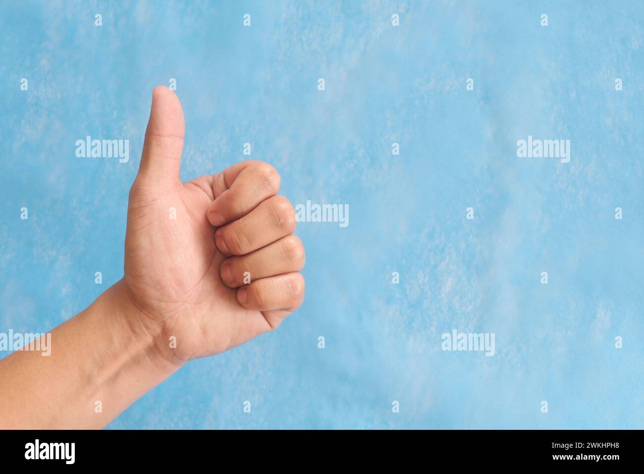 Junge männliche asiatische Hand macht Daumen hoch Schild isoliert auf blauem Hintergrund. Stockfoto