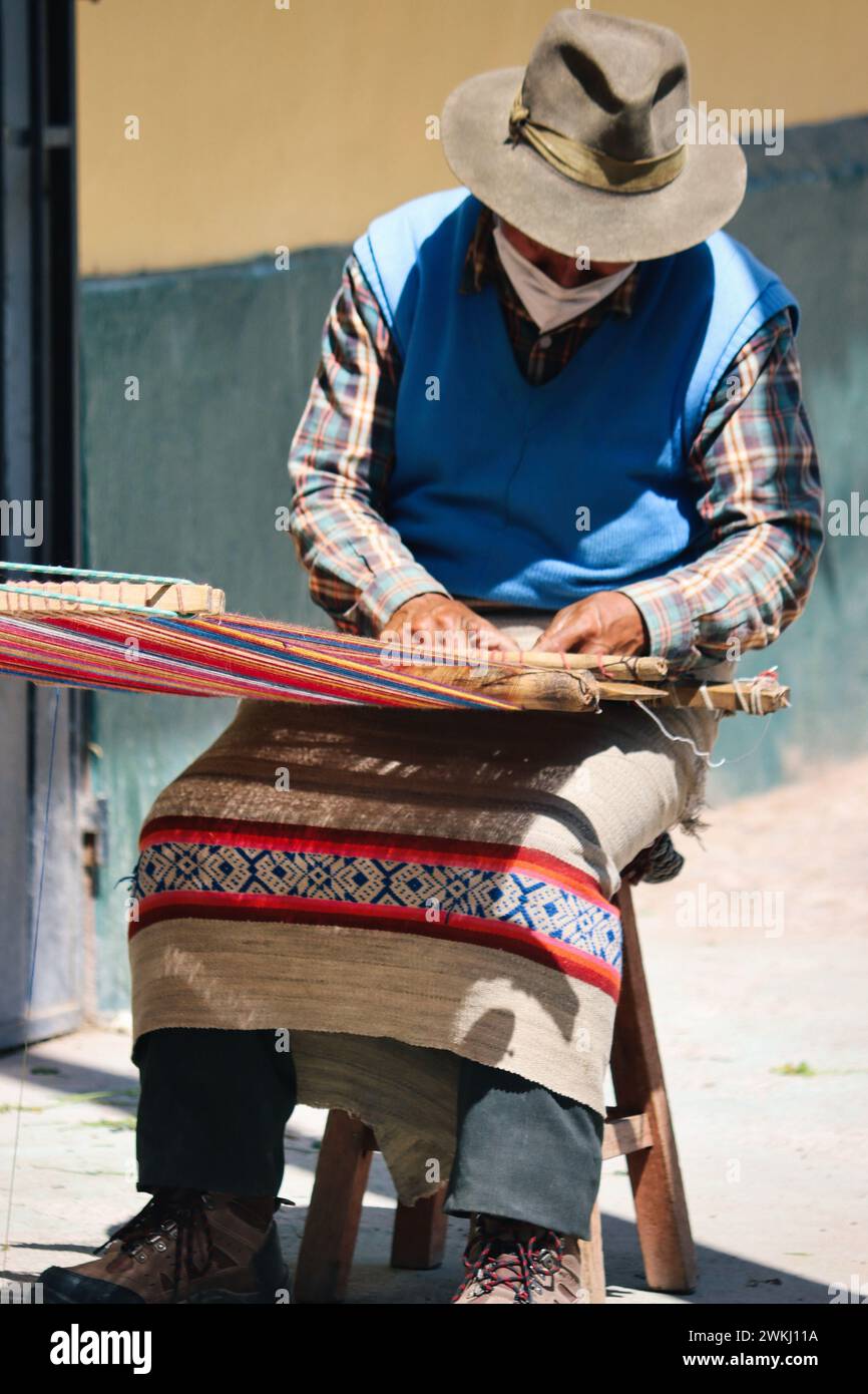 Dieses Foto im Herzen Perus zeigt einen erfahrenen peruanischen Handwerker, der einen traditionellen Hut trägt, während er akribisch einen pulsierenden peruanischen Kunsthandwerker herstellt Stockfoto