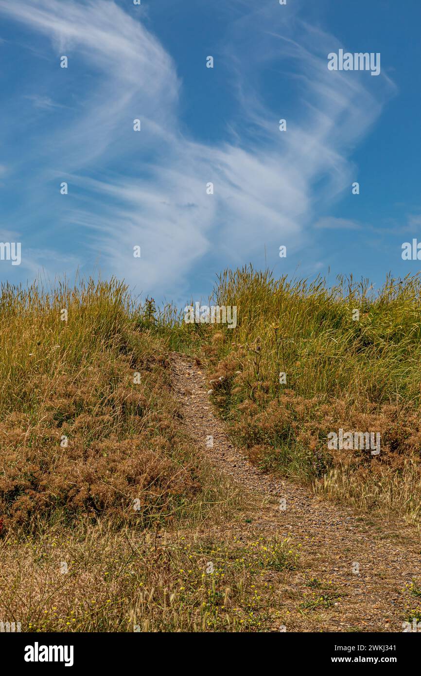 Ein Küstenweg an einem Kieselstrand mit blauem Himmel über dem Meer Stockfoto