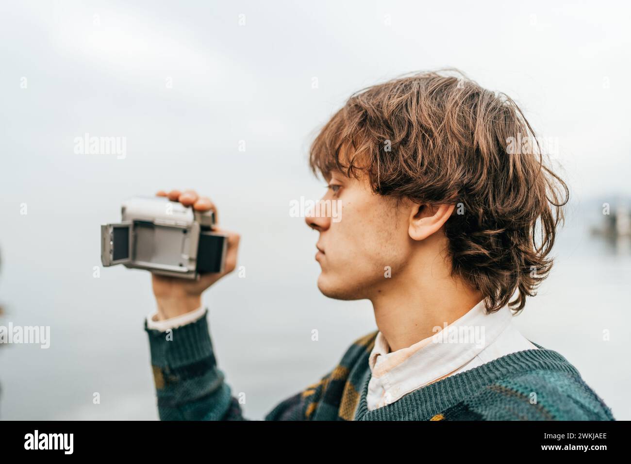 Junger Fotograf, der Momente mit einer Vintage-Kamera am See festnimmt. Stockfoto