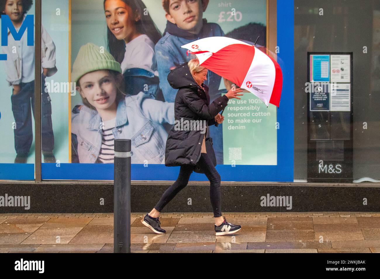 Frau mit rot-weißem Golfschirm in Preston, Lancashire. Wetter in Großbritannien. Februar 2024. Starke Winde und starker Regen für Käufer im Stadtzentrum. Credit; MediaWorldImages/AlamyLiveNews Stockfoto