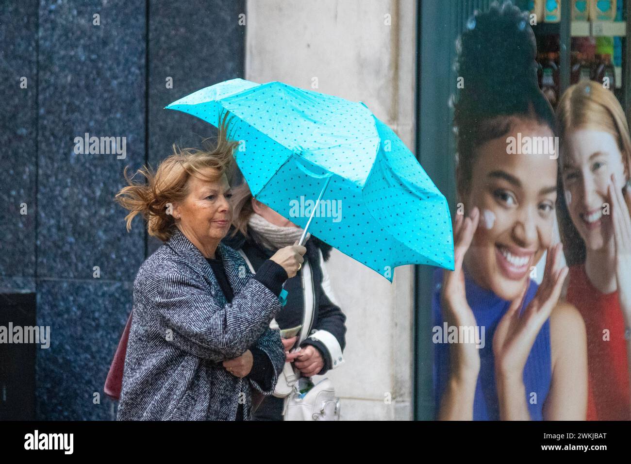 Frau mit blauem und weißem Schirm an einem regnerischen Tag in Preston, Lancashire. Wetter in Großbritannien. Februar 2024. Starke Winde und starker Regen für Käufer im Stadtzentrum. Credit; MediaWorldImages/AlamyLiveNews Stockfoto