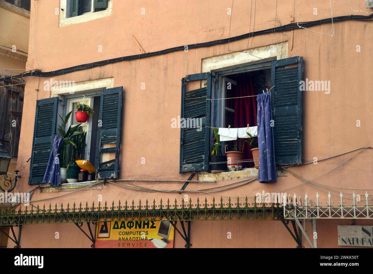 Waschen hängt an der Wäscheleine vor grünen Fenstern über den Geschäften in der Altstadt von Korfu, Griechenland, EU. Stockfoto