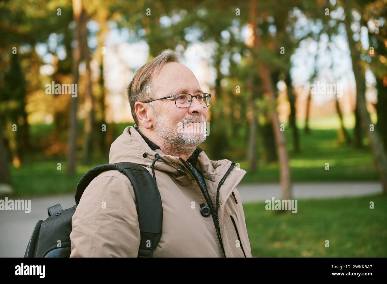 Außenporträt eines gutaussehenden Mannes mittleren Alters im grünen Park mit warmer Jacke und Rucksack Stockfoto