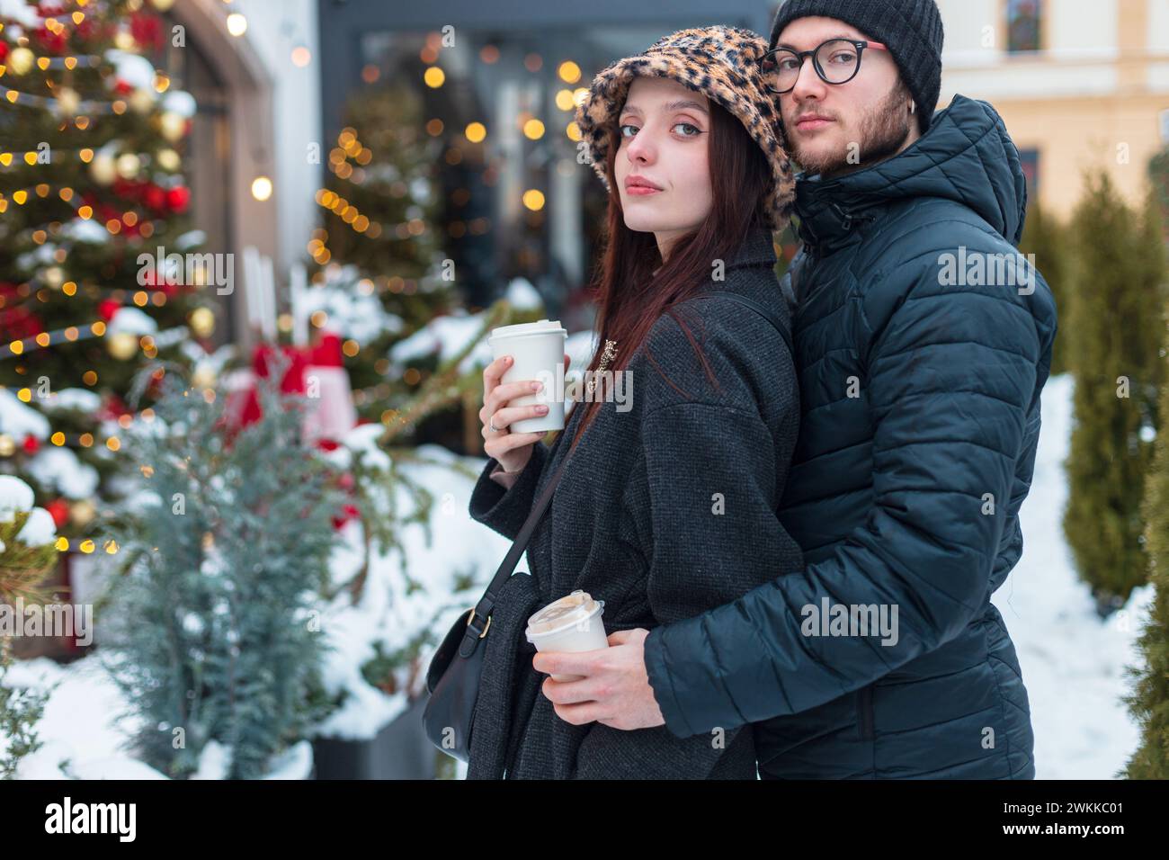 Glückliche, schöne junge Modefreunde in modischer Winterjacke, die Kaffee hält, umarmt und mit chris in der Stadt spaziert Stockfoto